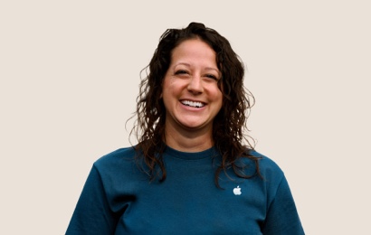 ウェーブがかかった黒いロングヘアのApple Retailチームメンバーが笑顔を浮かべているポートレート。